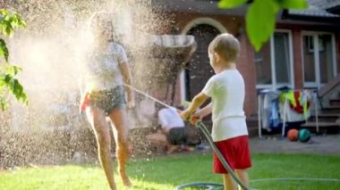 Slow motion video of little toddler boy splashing water on his elder sister from garden hose