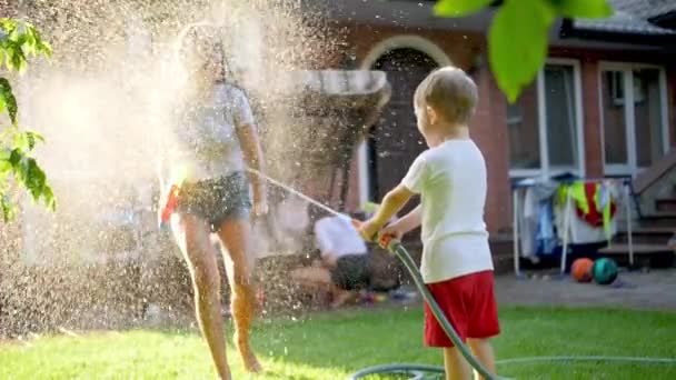 Slow motion video of little toddler boy splashing water on his elder sister from garden hose — Wideo stockowe