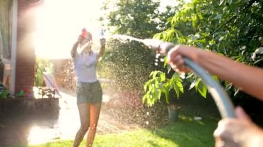 Slow mtoion video of two teenage girls splashing water from water guns and garden hose at each other