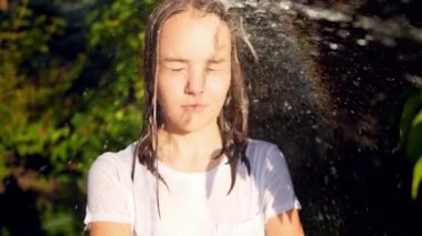 Slow motion video of splashing water from garden hose in teenage girls face at garden