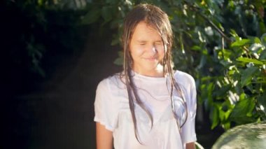 Closeup slow motion video of pouring water from bucket on smiling teenage girl in the garden at hot summer day
