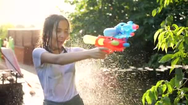 Slow motion closeup video of wet teenage girl shooting water from toy gun during water fight at backyard — 비디오