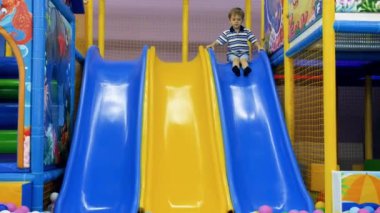 4k video of 4 years old little boy sliding down in the pool full of colorful plastic balls in amusement park