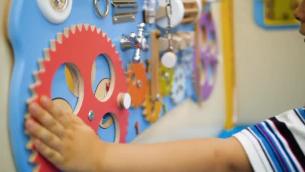 Closeup 4k video of little toddler boy playing with ropes wooden gears on valves on educational board at museum of science — Stok video