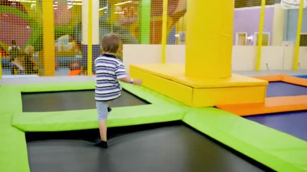 4k video de niño alegre corriendo y saltando en camas elásticas en parque de atracciones para niños en el centro comercial — Vídeos de Stock