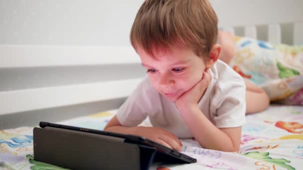 4k video de lindo niño acostado en la cama y navegar por Internet en la tableta digital — Vídeos de Stock