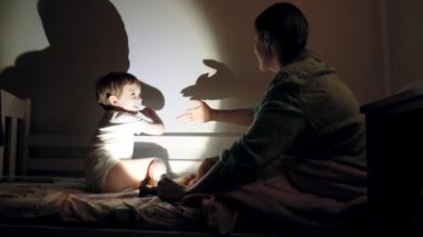 4k video of little smiling boy playing with shadows on the wall from torch in bedroom at night