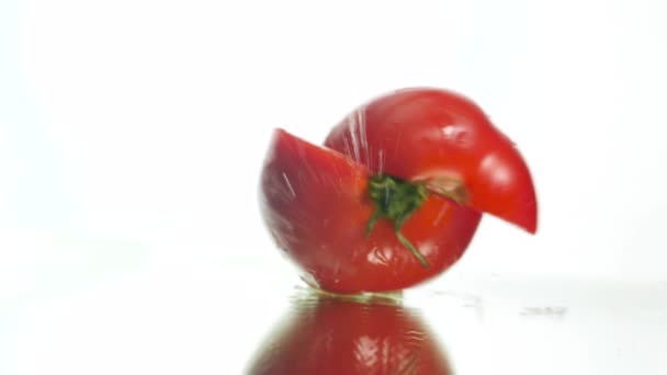 Closeup slow motion video of fresh red tomato falling on wet reflective surface and splitting in two slices. Concept of healthy nutrition and organic food. Perfect background for vegetarian or vegan — Wideo stockowe