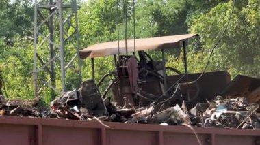 4k video of big crane with electric magnet lifting metal scrap and loading it in high pressure recycling machine on the scrapyard