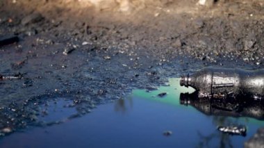 4k dolly video of plastic bottle lying in black oil or diesel waste pubble on the ground. Concept of ecology disaster and industrial damage to nature