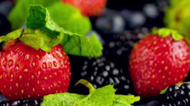 4k 'lık kameranın büyük çeşit böğürtlen ve nane yaprakları üzerinde hareket ettiğini gösteren bir video. Bir yığın çilek, yabanmersini ve böğürtlen. Organik gıda ve sağlıklı beslenme için mükemmel soyut bir arka plan..