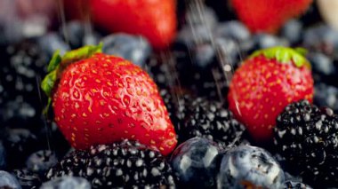 Masada duran taze çilek, yabanmersini ve böğürtlen üzerine düşen su damlacıklarının makro yavaş çekim videosu. Organik yiyecekler ve sağlıklı beslenme için mükemmel bir soyut çekim. Böğürtlen yakın çekim
