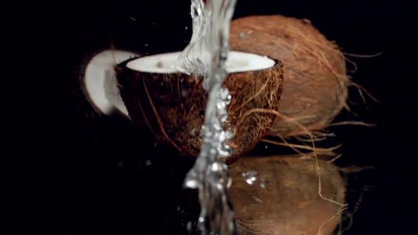 Primer plano video en cámara lenta de la mitad de coco lleno de leche o agua que cae sobre la superficie negra y salpicaduras. Perfecto tiro abstracto para alimentos orgánicos y una nutrición saludable . — Vídeos de Stock