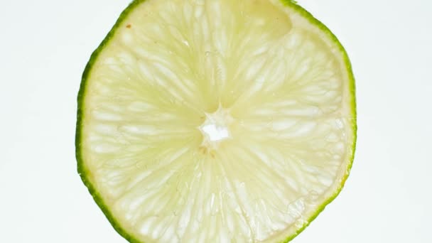 Vídeo macro de rodajas de lima o limón exprimidas sobre fondo blanco. El jugo fluye lentamente de la rebanada. Fondo abstracto perfecto para alimentos orgánicos y una nutrición saludable . — Vídeo de stock