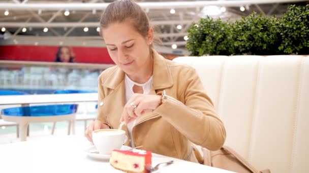 4k beeldmateriaal van jonge lachende vrouw zit in cafe opent papieren zak met suiker, gieten in een kopje koffie en drinken — Stockvideo
