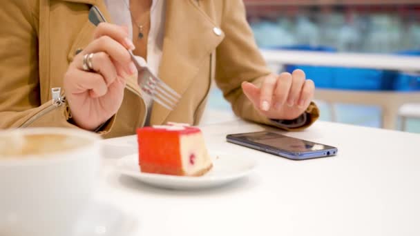 4k video de la joven sentada en la cafetería, comiendo delicioso postre dulce y la navegación de fotografías en las redes sociales utilizando el teléfono inteligente — Vídeo de stock