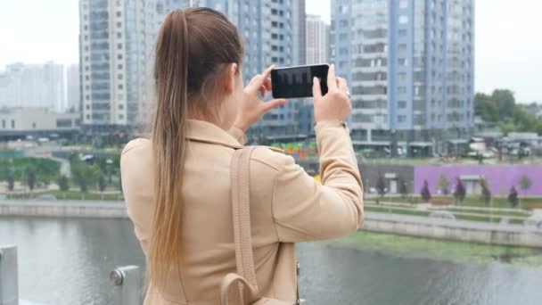 4k video of young woman standing on the rooftop and making photographs on smartphone of skyline and city — Stock Video