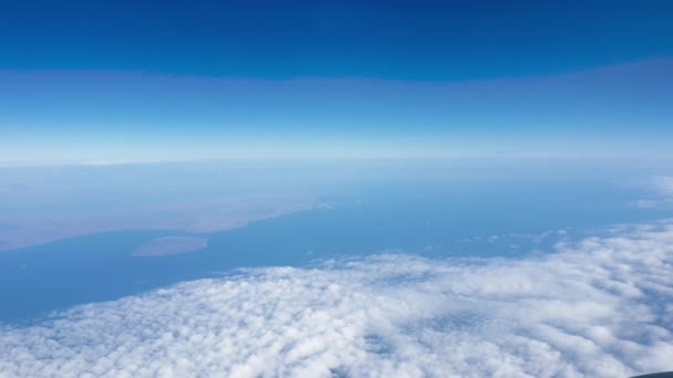 4k video of airplane flying above the ocean and land covered with clouds — Stock Video