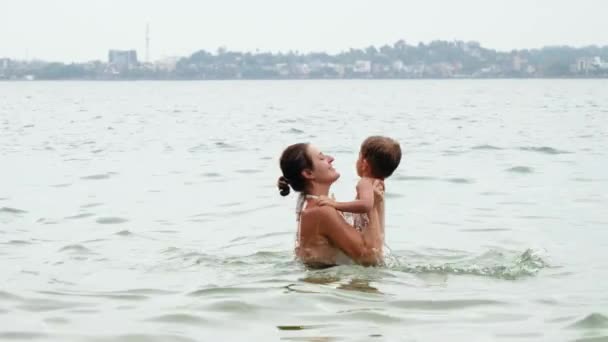 4k footage of happy smiling mother embracing and throwing up her little son while swimming in ocean — Stock Video