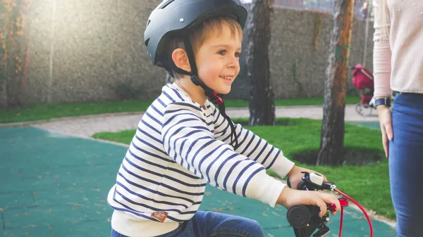 검은 보호 헬멧을 쓰고 자전거를 타고 있는 명랑하게 웃고 있는 어린 소년의 사진이 찢어 져 있다 — 스톡 사진