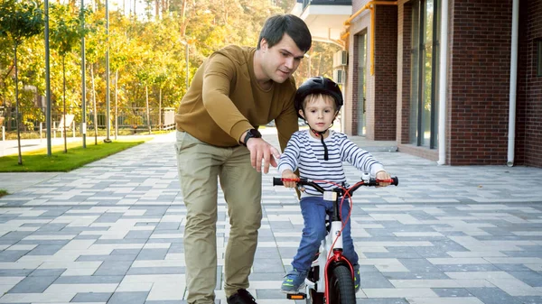 彼の小さな息子を教えるハンサムな若い男彼の最初の自転車に乗って公園で — ストック写真