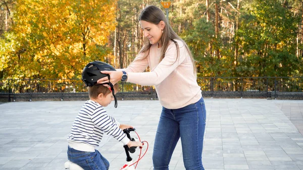 Portret pięknej młodej kobiety zakładającej kask ochronny na syna przed nauką jazdy na rowerze — Zdjęcie stockowe
