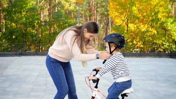 Piękna uśmiechnięta kobieta dopasowująca i zapięta klamra na hełmie na głowie syna jeżdżąca na rowerze — Zdjęcie stockowe