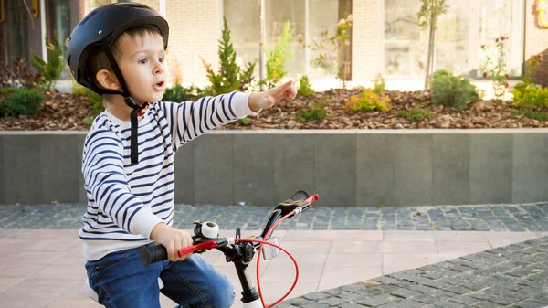 Retrato de niño montado en bicicleta excitado y señalando con el dedo — Foto de Stock