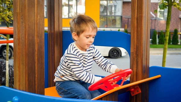 Portret małego chłopca bawiącego się na placu zabaw w drewnianym samochodziku — Zdjęcie stockowe