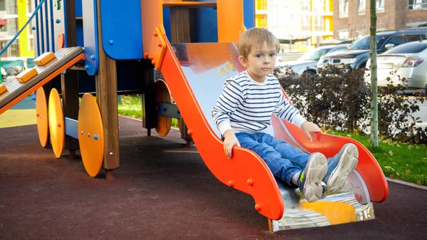 Zdenerwowany chłopczyk siedzący na zjeżdżalni na placu zabaw dla dzieci — Zdjęcie stockowe