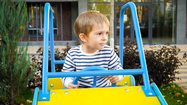 Glücklich lächelnder Junge reitet in großem Spielzeugauto auf Kinderspielplatz — Stockfoto