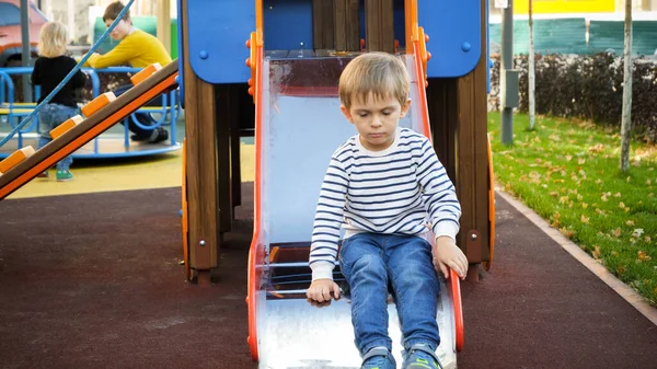 Sorglig och upprörd liten ensam pojke sitter på rutschkana på lekplatsen — Stockfoto