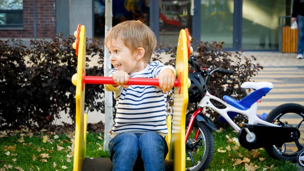 Portrait of happy laughing little boy riding on children playground at park — Stock Photo, Image