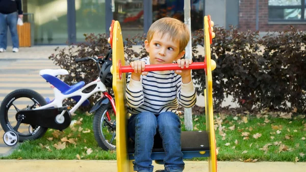 Portret troskliwego chłopca siedzącego na placu zabaw w parku — Zdjęcie stockowe