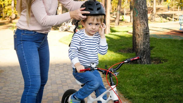 Zbliżenie zdjęcie młodej troskliwej kobiety zakładającej kask ochronny na syna jeżdżącego na rowerze — Zdjęcie stockowe