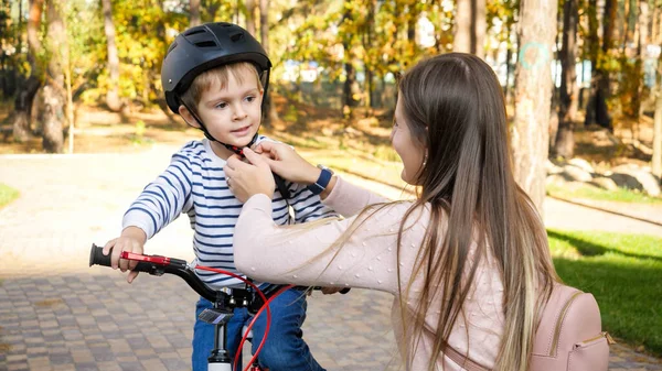 Portret pięknej młodej matki dopasowującej kask bezpieczeństwa na głowie swoich synów przed jazdą na rowerze w parku — Zdjęcie stockowe