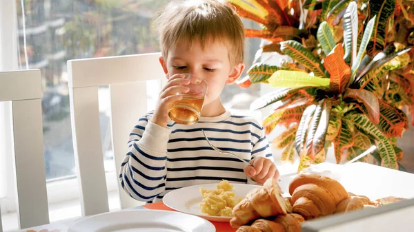 Cute 3 years old boy drinking apple juice from glass during dinner in dining room — Stock Photo, Image