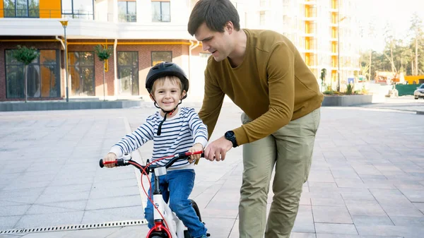 Portrait d'un petit garçon souriant apprenant à monter son premier vélo avec son jeune père — Photo