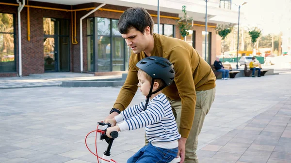 Młody ojciec wspiera swojego synka ucząc jazdy na rowerze — Zdjęcie stockowe