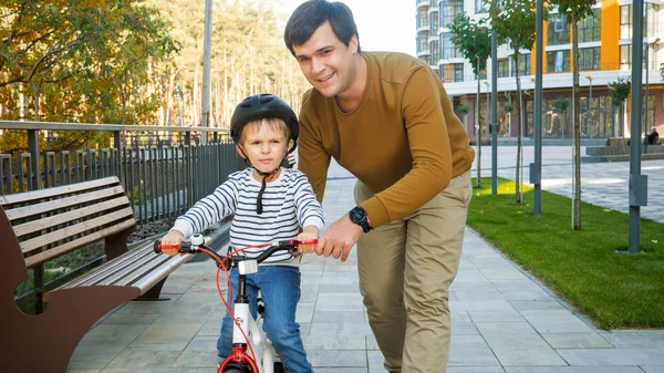 Портрет счастливого улыбающегося человека, обучающего своего сына кататься на первом велосипеде — стоковое фото