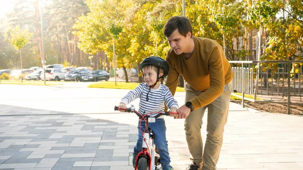 Portrait de jeune homme soutenant et tenant son petit fils apprenant à faire du vélo au parc — Photo