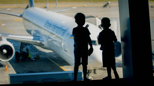 Silhueta de dois meninos loking através da janela no avião no terminal do aeroporto — Fotografia de Stock