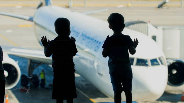 Silhouetten von zwei kleinen Jungen, die vor dem Flug durch ein Fenster in das Flugzeug schauen — Stockfoto