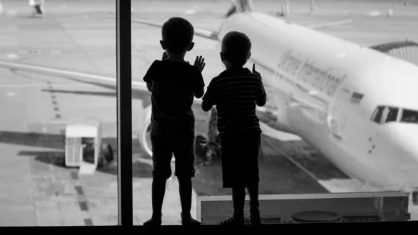 Schwarz-Weiß-Bild von Jungen-Silhouetten, die auf ein großes Flugzeug blicken, das im Flughafenterminal geparkt ist — Stockfoto