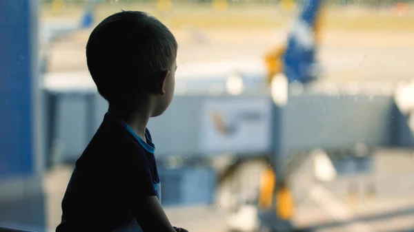 Toned portrait of sad little boy looking through window on big airplane in airport — Stock Photo, Image