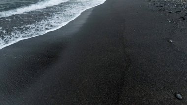 Kıyıdaki ıslak siyah volkanik kumda yuvarlanan okyanus dalgalarının soyut görüntüsü