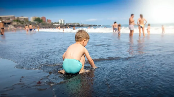 Cute little boy siedzi na plaży oceanu i czeka na fali morskiej — Zdjęcie stockowe