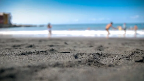 Blurred out of focus photo of black volcanic sand on ocean beach — Stock Photo, Image