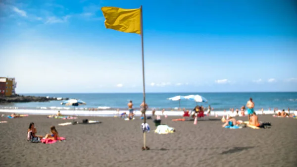 Blurred out of focus iamg eof yellow flag on the ocean beach and sunny windy day — Stock Photo, Image