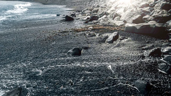 Θαλασσινό τοπίο από λαμπερό ήλιο λάμπει σε μαύρη ηφαιστειακή παραλία της θάλασσας και μπλε κύματα του ωκεανού — Φωτογραφία Αρχείου